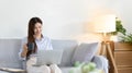 Beautiful Asian woman working on laptop and sipping coffee with smiling face in her home Royalty Free Stock Photo