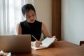 A beautiful Asian woman working remotely at a coffee shop is writing some ideas down in her book Royalty Free Stock Photo