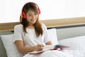 Beautiful asian woman writing diary on the bed in bedroom. She is siting on white bedding. Royalty Free Stock Photo