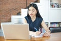 Beautiful Asian woman writing a notebook on table with laptop aside.