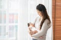 Beautiful Asian woman holding newborn baby in her arms standing in front of windows at cozy home.Happy infant baby sleep in mother Royalty Free Stock Photo