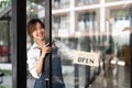 Beautiful asian young barista woman in apron holding tablet and standing in front of the door of cafe with open sign Royalty Free Stock Photo