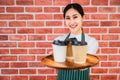 Beautiful asian young barista woman in apron holding tray coffee with serving to customer in cafe Royalty Free Stock Photo