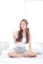 Beautiful asian young woman enjoy listen music with headphone and holding smart mobile phone while sitting in bedroom Royalty Free Stock Photo