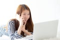 Beautiful asian young woman lying on bed using laptop and talking mobile smart phone at bedroom for leisure and relax Royalty Free Stock Photo