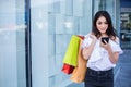 Beautiful asian young woman with shopping bags using her smart phone with smile while standing at the clothing store. Happiness, Royalty Free Stock Photo