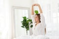 Beautiful Asian young Woman stretching her arm after wake up on bed and looking outside windows in cozy bedroom feeling so fresh Royalty Free Stock Photo