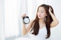 Beautiful asian young woman wake up in morning annoyed alarm clock holding hand Royalty Free Stock Photo