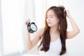 Beautiful asian young woman wake up in morning annoyed alarm clock holding hand. Royalty Free Stock Photo