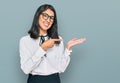 Beautiful asian young woman wearing business shirt and glasses amazed and smiling to the camera while presenting with hand and Royalty Free Stock Photo