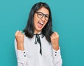 Beautiful asian young woman wearing business shirt and glasses screaming proud, celebrating victory and success very excited with Royalty Free Stock Photo