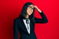 Beautiful asian young woman wearing business suit very happy and smiling looking far away with hand over head Royalty Free Stock Photo