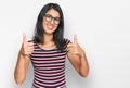 Beautiful asian young woman wearing casual clothes and glasses approving doing positive gesture with hand, thumbs up smiling and Royalty Free Stock Photo