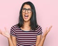 Beautiful asian young woman wearing casual clothes and glasses crazy and mad shouting and yelling with aggressive expression and Royalty Free Stock Photo