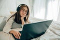 Beautiful asian young woman wearing headphones listening music or watching movie with laptop on the white bed Royalty Free Stock Photo