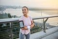 Beautiful sportswoman in sportswear smiles toothy smile standing with crossed arms on the city bridge, ready for morning jog at