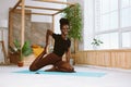 Beautiful and athletic afro american woman sitting with smile and pulling bent rear leg, doing yoga on gym mat in