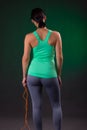 Beautiful athletic, fitness woman standing, posing with a jump rope on a gray background with a green backlight Royalty Free Stock Photo