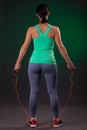 Beautiful athletic, fitness woman standing, posing with a jump rope on a gray background with a green backlight Royalty Free Stock Photo