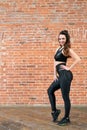 Beautiful athletic girl in a black sports top and leggings posing against a brick wall Royalty Free Stock Photo