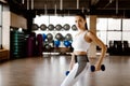 Beautiful athletic girl dressed in white sports top and tights builds up muscles with dumbbells Royalty Free Stock Photo