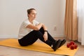 Beautiful athletic slim bored sportswoman wearing white T-shirt and black leggins with hair bun looking away with sad upset Royalty Free Stock Photo