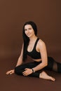 A beautiful athletic woman, fitness trainer or yogi, sits on a brown background in the studio after a workout and smiles