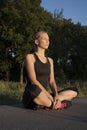 Beautiful athletic young adult woman is taking a break during outdoor exercising, sitting cross legged Royalty Free Stock Photo