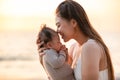 Beautiful Attractive Asian mom holding her baby newborn in hand and kissing on baby head sweet and lovely outdoor on the beach. Royalty Free Stock Photo