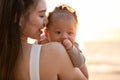 Beautiful Attractive Asian mom holding her baby newborn in hand and kissing on baby head sweet and lovely outdoor on the beach. Royalty Free Stock Photo