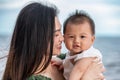 Beautiful Attractive Asian mom holding her baby newborn in hand and kissing on baby head sweet and lovely outdoor on the beach. Royalty Free Stock Photo