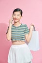 Beautiful Attractive Asian Woman holding shopping bags and calling with mobile phone isolated on pink background Royalty Free Stock Photo