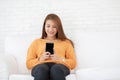 Beautiful Attractive Asian woman sitting on white sofa using smartphone in living room Royalty Free Stock Photo