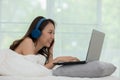 Beautiful Attractive Asian young woman listen music and lying on bed looking on computer laptop in bedroom feeling so relax and co Royalty Free Stock Photo