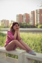 Beautiful and attractive woman sitting on a river concrete side, wearing casual denim shorts