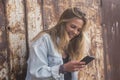 Beautiful and attractive woman teenager using her phone alone in a city with urban wall at the background - blonde lady chatting Royalty Free Stock Photo