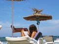 Beautiful Attractive Young Girl with Long Hair Sitting Relaxing and Reading Book under Straw Beach Parasol Umbrella and Blue Sky Royalty Free Stock Photo