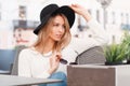 Beautiful attractive young woman in a knitted white sweater in jeans in a stylish elegant hat sitting on a sofa at a gray table Royalty Free Stock Photo