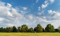 A beautiful August day in the park. A green field, a few trees in the distance under a beautiful blue sky sprinkled with clouds Royalty Free Stock Photo