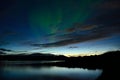Beautiful aurora borealis dancing over calm fjord and mountains