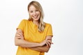 Beautiful authentic blond girl, smiling woman cross arms on chest, posing in yellow t-shirt, standing over white