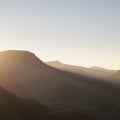 Beautiful Autumn Fall landscape image of sun beams lighting up small area of mountain side in Lake District whilst rest of area is