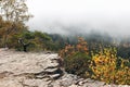 Beautiful autumn misty landscape, scenic view. Fog above forest valley. Rocky hills, pine and birch trees with colorful Royalty Free Stock Photo