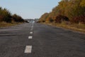 Beautiful autumn road. Autumn background. Country road made of old asphalt among beautiful trees with yellow and orange