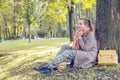 Beautiful autumn woman sitting near tree outdoors. Romantic girl in fall park Royalty Free Stock Photo