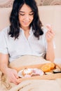 Beautiful awesome dark haired woman having tasty breakfast in bed at her cozy bedroom. Side view photo of young girl in blue Royalty Free Stock Photo