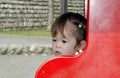 Beautiful baby Asian girl outdoors in public park with thoughtful look. Defocused background with stone wall Royalty Free Stock Photo