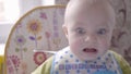 Beautiful baby boy at the table take a cookie in his hand, eating it, watching into the camera and babbling close up Royalty Free Stock Photo