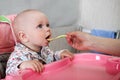 Beautiful baby eats porridge from mom's hand. He is sitting on a pink children' chair. Royalty Free Stock Photo