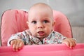 Beautiful baby eats porridge from mom's hand. He is sitting on a pink children' chair. Royalty Free Stock Photo